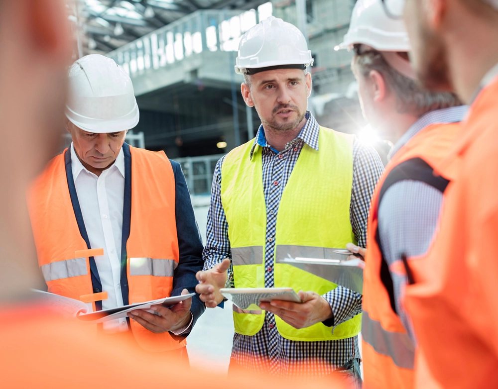 Site lead reviewing safety documents with a team in hard hats and high-visibility vests